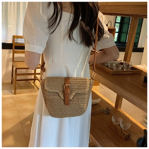 Detail der gewebten Strohtasche mit braunem Lederriemen getragen von Model im weißen Kleid