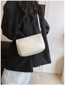 Détail du sac bandoulière crème avec logo LUKADI BAG et surpiqûres sur un blazer noir