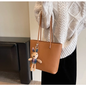 Brown leather tote bag with a cute plush bunny pendant shown on a model's shoulder