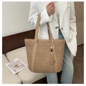 Detail of woven straw tote bag featuring decorative beaded tassels and textured shoulder straps