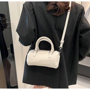 Detailed view of cream-white cylinder Boston bag with vertical embossed texture and strap