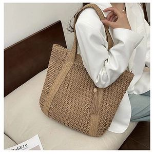 Fashionable woven straw tote bag with tassel charm carried by a model in casual attire