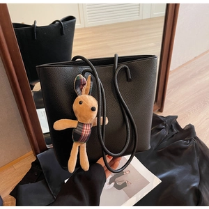 Detail of black pebbled leather tote bag with cute plush rabbit charm in casual home setting