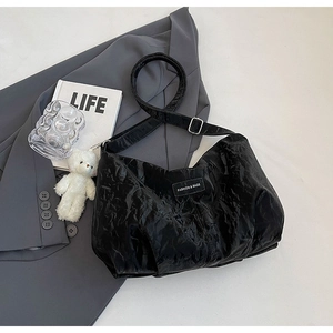 Detail of black pleated tote bag featuring a branded label and silver metal buckle