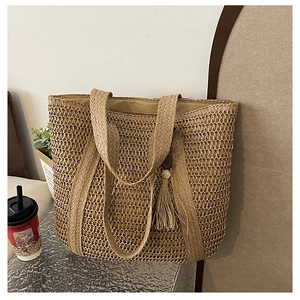 Detailed close-up of khaki woven straw tote bag with decorative tassel and shoulder straps