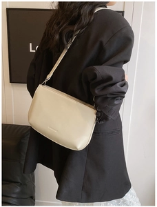 Détail du petit sac bandoulière crème porté avec un costume noir pour un style chic