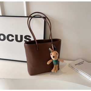 Detail of deep brown leather tote bag featuring a cute bunny plush charm on a white desk