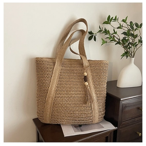 Detail of hand-woven straw tote bag with decorative wooden bead tassel on a wooden shelf