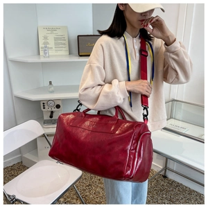 Large red travel bag in shiny oil wax leather with adjustable strap shown on model