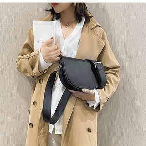 Close-up of black leather saddle bag with silver buckle and wide strap on model