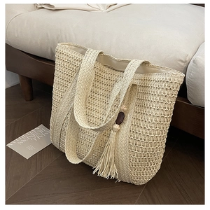 Detailed close-up of woven straw tote bag texture with wooden bead tassel charm