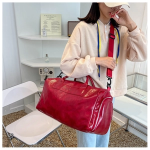 Detailed view of red large capacity travel bag in glossy PU leather on a shoulder