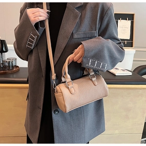 Close-up of beige pleated cylinder handbag with silver hardware and shoulder strap