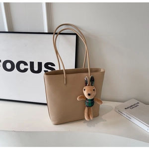 Detailed close-up of beige lychee grain leather tote bag with cute plush rabbit charm