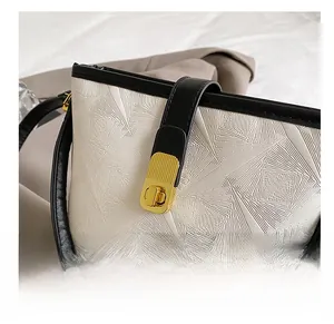 Close-up of golden twist lock and geometric embossed texture on cream bucket bag