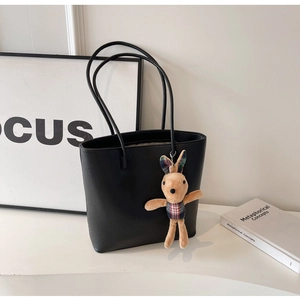 Detail view of black lychee grain leather tote bag with a cute plush rabbit charm