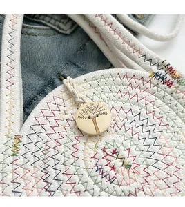 Detail of white cotton rope bag with colorful wavy stitching and a carved wood button