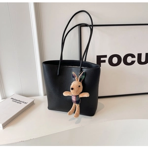 Close-up of black lychee grain tote bag featuring a cute plush bunny charm on the handle