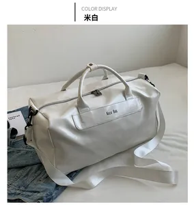 Detail of a large cream PU leather travel bag with adjustable strap on a white bed