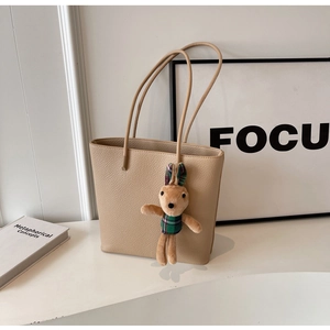 Detail of beige lychee grain leather tote bag featuring a cute bunny plush charm
