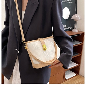Detail view of a white textured bucket bag with beige leather trim and a gold twist lock