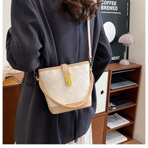 Crossbody shot of cream bucket bag with radial textures and golden twist lock