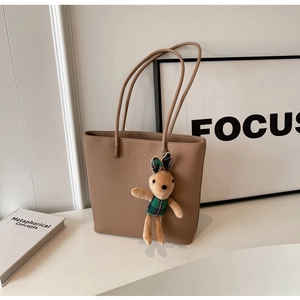Detail of lychee pattern leather tote bag with a cute plush bunny charm on white stand
