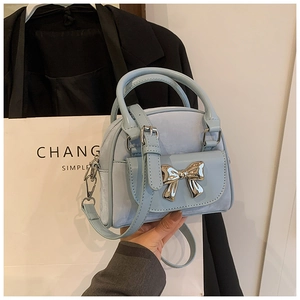 Close-up of light blue mini shell bag with golden bow hardware and suede leather texture