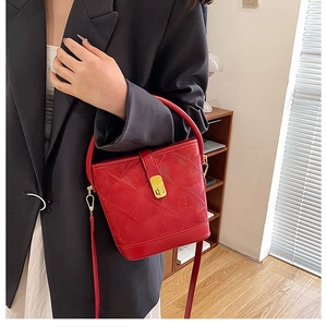 Detail of red embossed bucket bag with gold clasp and wide strap on model