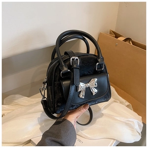 Detail of black velvet mini bag with silver metal bow and adjustable shoulder strap