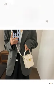 Vertical white textured crossbody bag with gold rivets shown on a stylish model