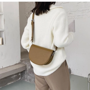 Close-up of a brown leather saddle bag with adjustable strap worn on a beige sweater