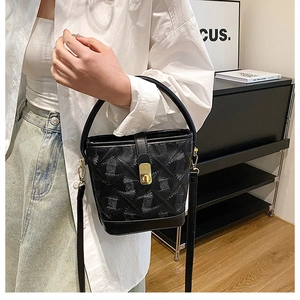 Detail of black bucket bag featuring quilted leather texture and golden metal buckle clasp