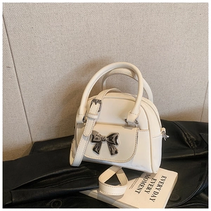 Detail of a creamy white bucket bag with silver metal bow clasp on a leather jacket