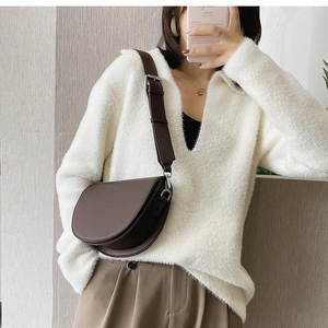 Detail of dark brown leather saddle bag with wide shoulder strap on white sweater outfit