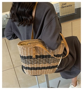 Detail of hand-woven straw tote with brown leather straps and black striped texture