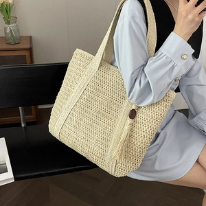 Large beige woven straw tote bag with decorative wooden bead tassel for beach vacation