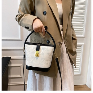 Detail of a white bucket bag with black accents and gold clasp held by a model