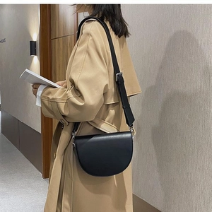 Detail of a black leather saddle bag with silver hardware worn over a khaki trench coat