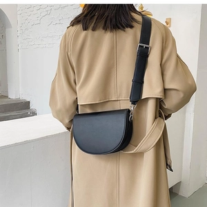 Rear view of model wearing a black semi-circular crossbody saddle bag over a beige coat