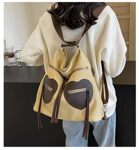 Detail view of large canvas backpack featuring heart-shaped pockets and long fringe tassels