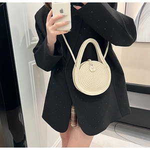 Detail of cream woven straw mini round bag featuring top handle and slim crossbody strap