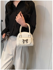 Detail of cream mini handbag featuring silver metallic bow and pearl finish leather