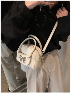 Detail of cream white mini crossbody bucket bag with silver metal bow and textured leather