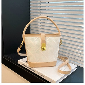 Detail of cream bucket bag with woven texture, leather trim and gold twist lock