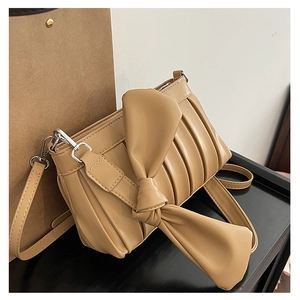 Dettaglio dell'elegante borsa a tracolla beige plissettata con un grande fiocco decorativo