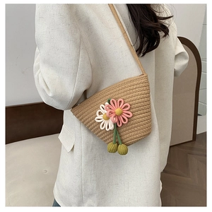 Detail of woven straw bucket bag featuring pink knit flowers and green pom-poms on model
