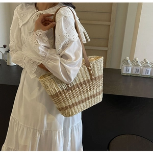 Detail of woven straw beach bag featuring brown leather straps and striped texture
