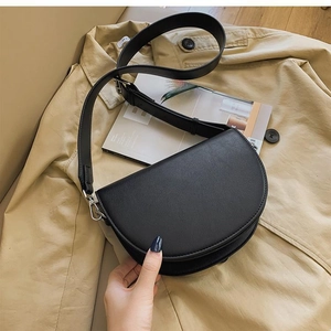Detail of black leather saddle bag with silver hardware on a khaki trench coat