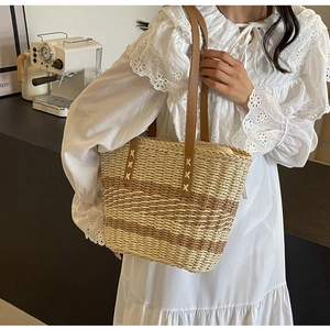 Detail of hand-stitched leather handles on a striped woven straw beach tote bag